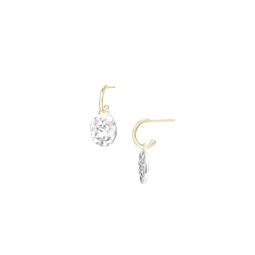 A pair of gold and silver drop earrings on a solid white background. One earring features a clear faceted teardrop gemstone in a gold hoop, while the other shows a silver disc charm with an engraved floral pattern attached to a gold hoop.