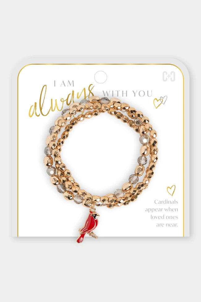 A three-strand beaded stretch bracelet set in rose gold and clear beads with a small red cardinal charm, displayed on a white jewelry card with gold lettering.