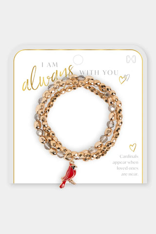 A three-strand beaded stretch bracelet set in rose gold and clear beads with a small red cardinal charm, displayed on a white jewelry card with gold lettering.