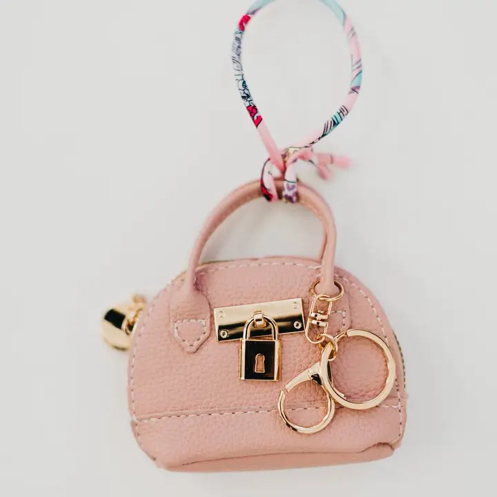 Pink purse-shaped keychain with gold lock and key design on a light gray background