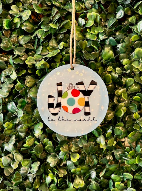 Decorative ornament with 'Joy to the world' text hanging on a green leafy background