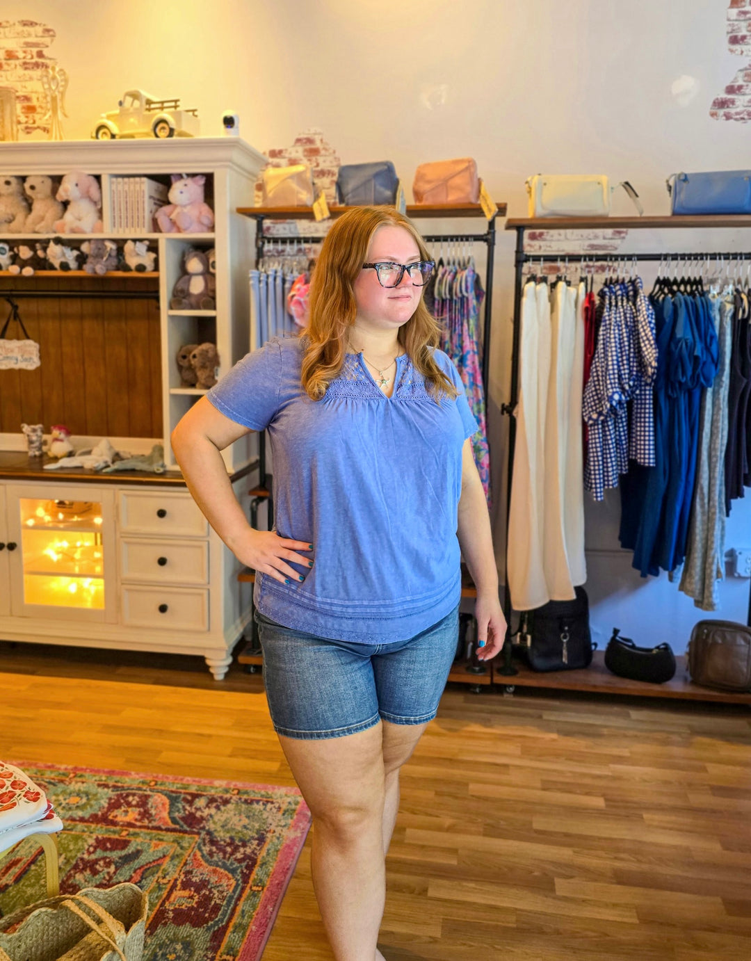 Woman in a blue shirt and denim shorts standing in a clothing store.