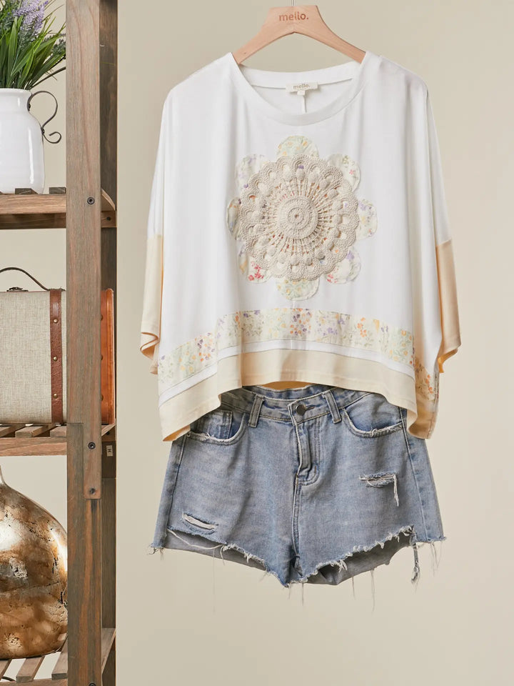 White blouse with floral design and denim shorts on a hanger against a neutral background