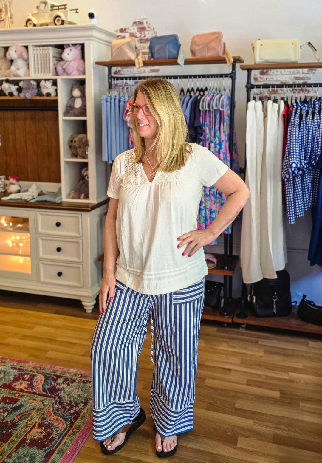 Woman standing in a clothing store with racks of clothes and shelves in the background.