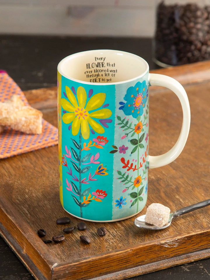 Colorful floral mug on a wooden surface with coffee beans and sugar.