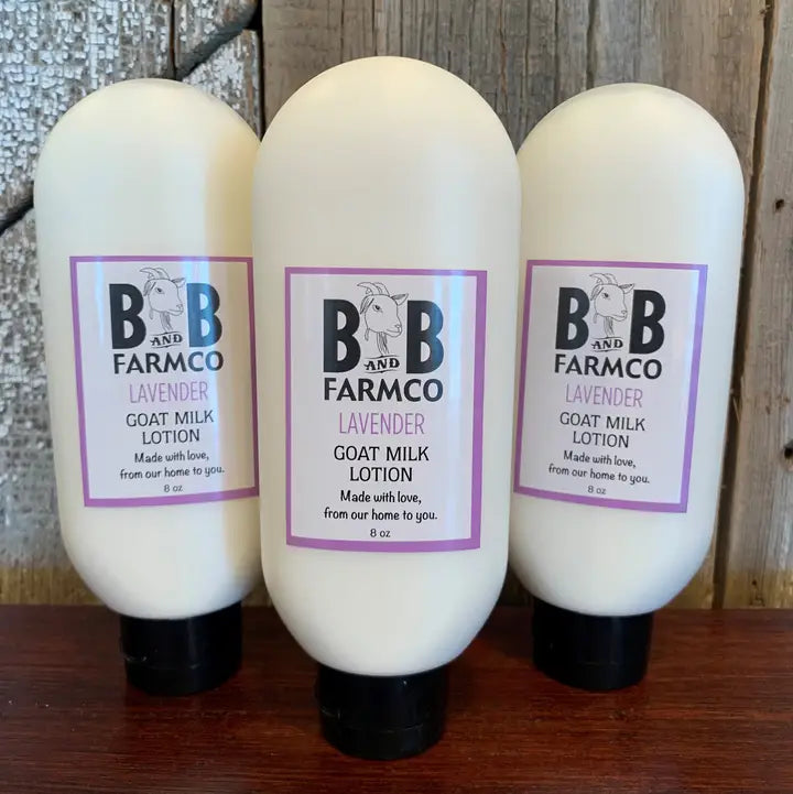 Three bottles of B&amp;B Farmco lavender goat milk lotion on a wooden surface.