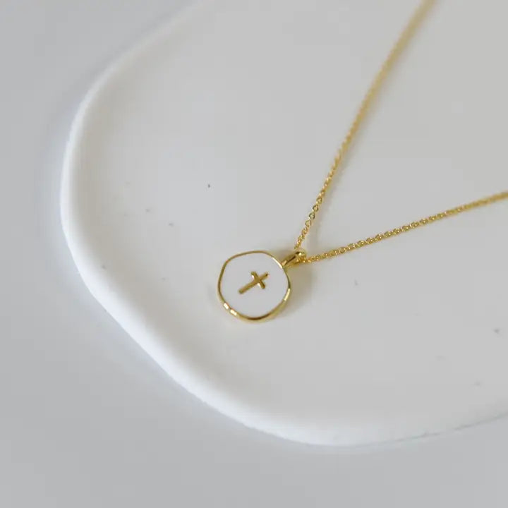 Gold necklace with a circular pendant featuring a cross on a white dish.