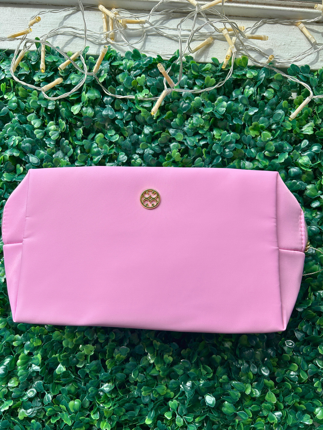 Pink clutch bag with a gold logo on a green textured surface