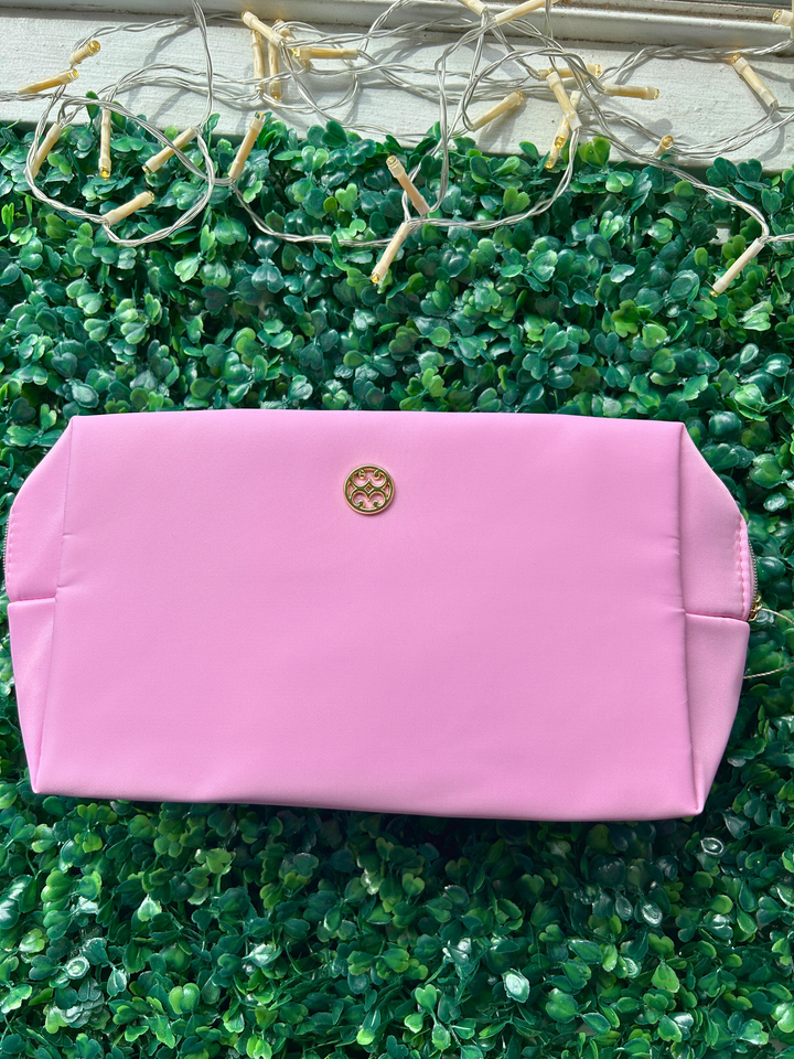 Pink clutch bag with a gold logo on a green textured surface
