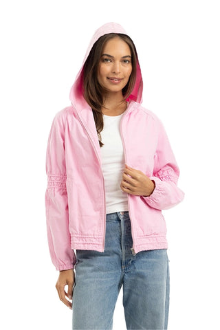 A woman wearing a light pink hooded jacket over a white t-shirt and blue jeans, standing against a plain white background.