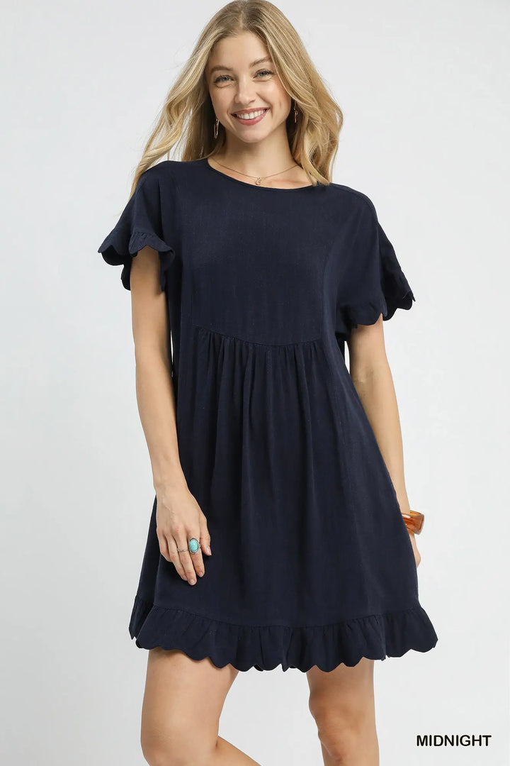 Woman wearing a navy blue dress with ruffled sleeves and hem on a white background