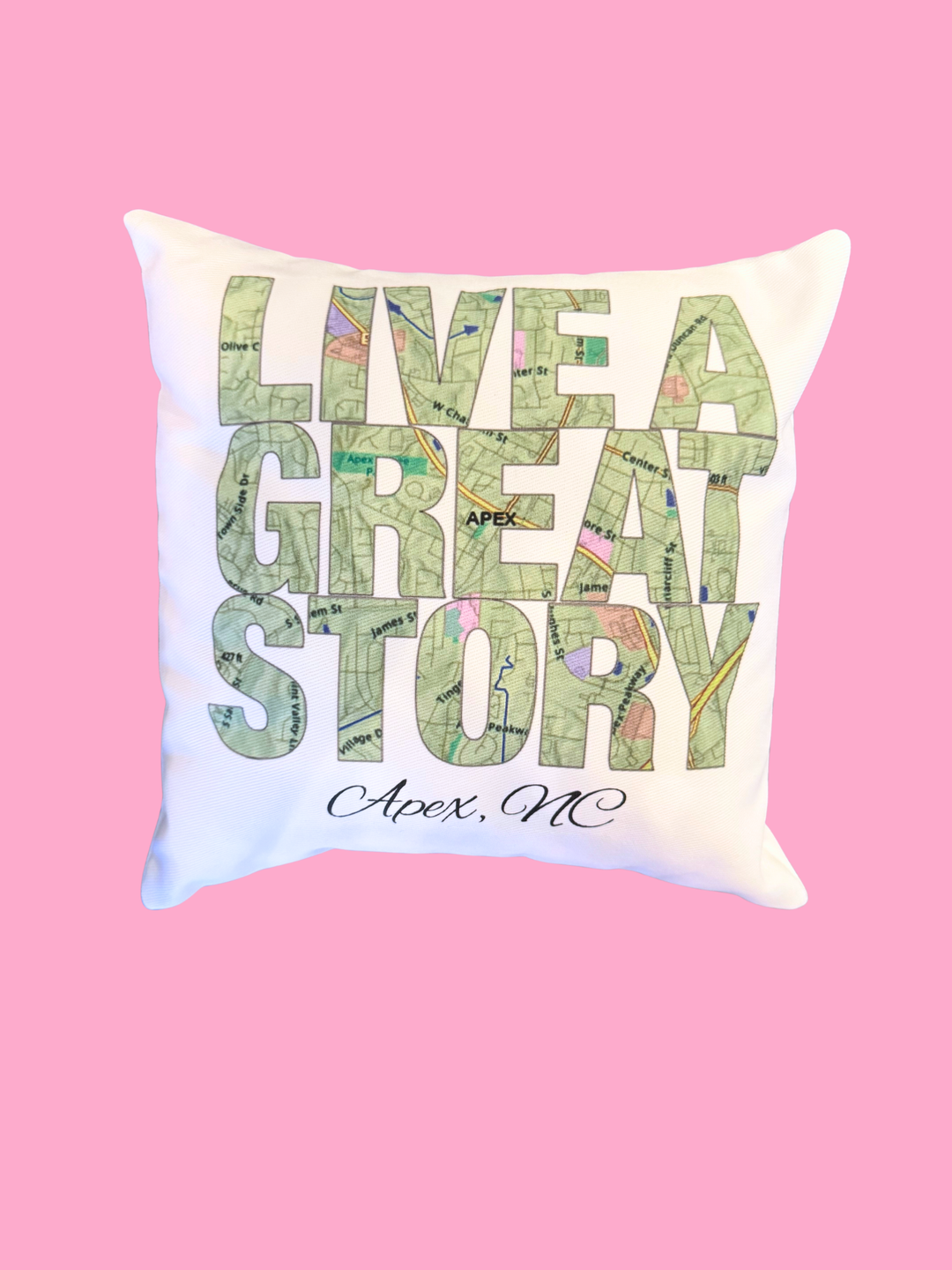 Decorative pillow with 'Live a Great Story Apex, NC' text on a pink background