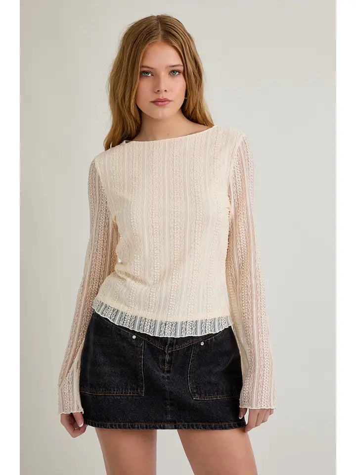 Woman wearing a cream sweater with sheer sleeves against a plain background