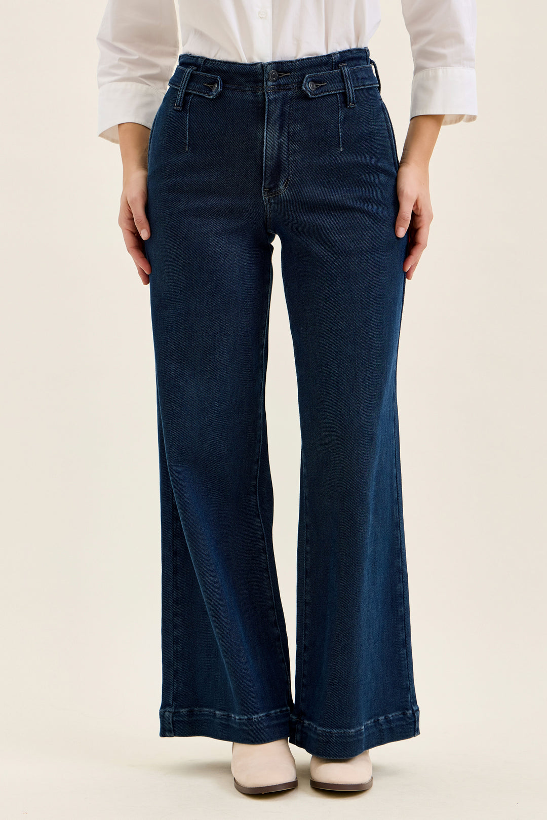 Person wearing dark blue wide-leg jeans on a beige background