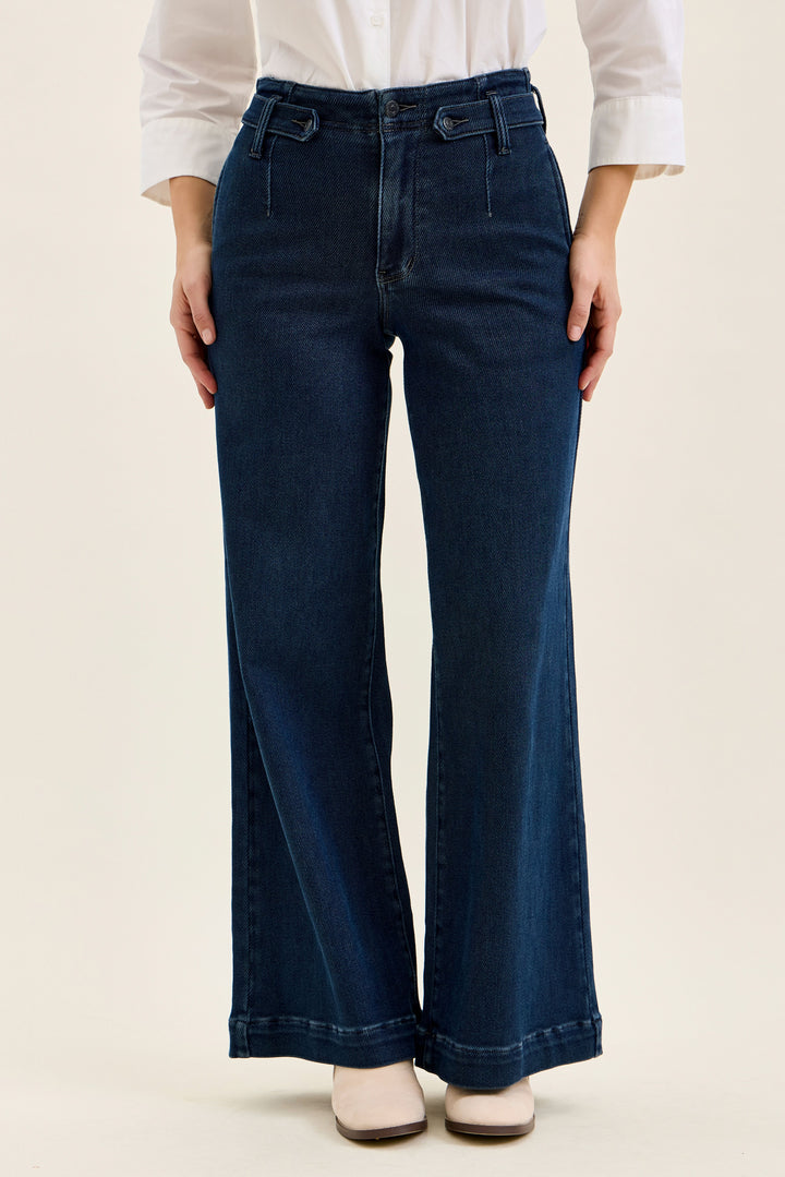Person wearing dark blue wide-leg jeans on a beige background