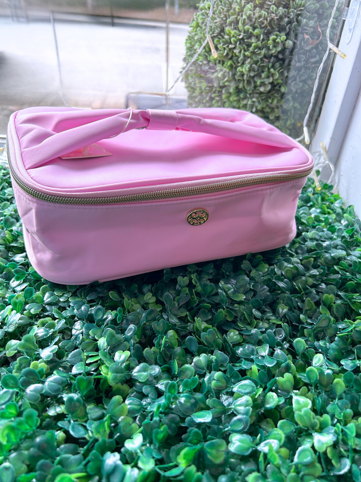 Pink makeup bag with gold zipper on a green textured surface