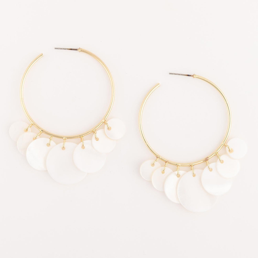 Gold hoop earrings with white beads on a light beige background