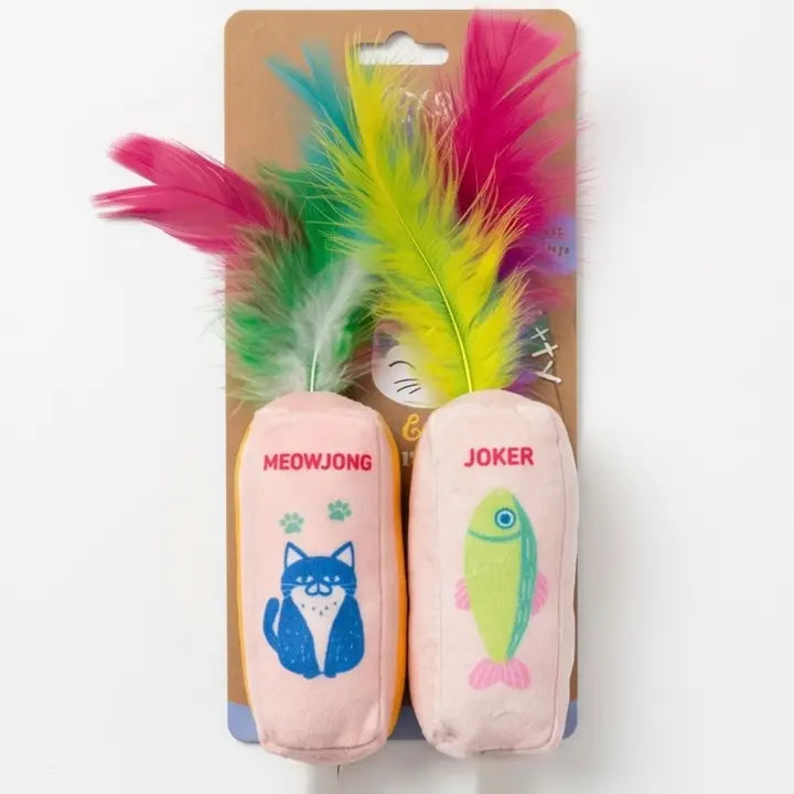 Two plush cat toys on a cardboard hanger with colorful feathers. One toy is light pink with a blue cat illustration and the text &