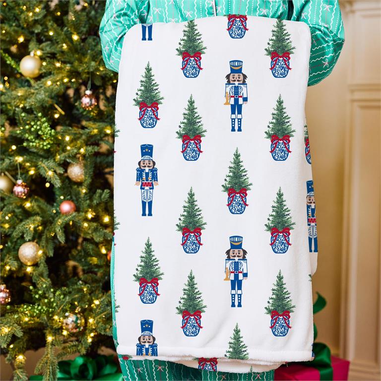 Person holding a Christmas-themed towel with tree and nutcracker pattern in front of a decorated tree.
