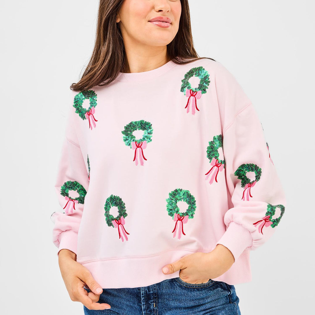 Person wearing a pink sweatshirt with green wreath patterns on a plain background