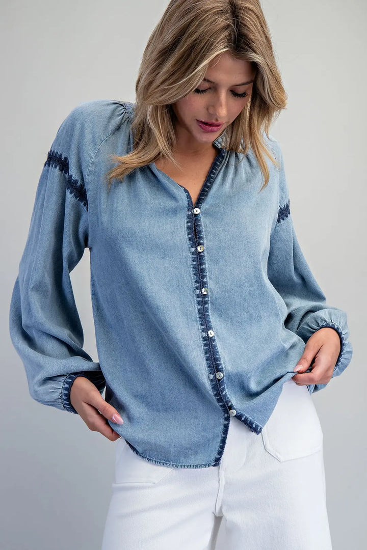 Woman wearing a light blue denim shirt with dark buttons against a plain background