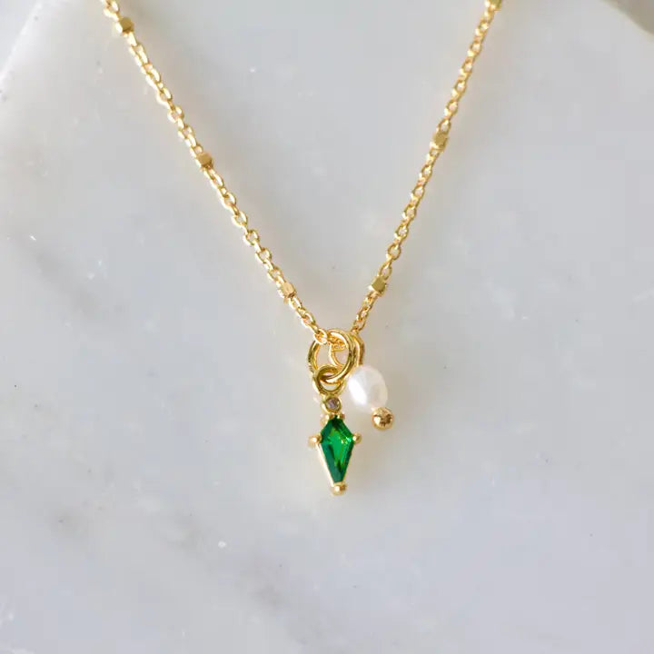 Gold necklace with green gemstone and pearl pendant on a light background