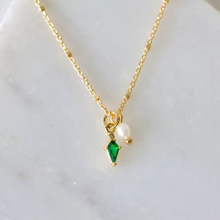 Gold necklace with green gemstone and pearl pendant on a light background