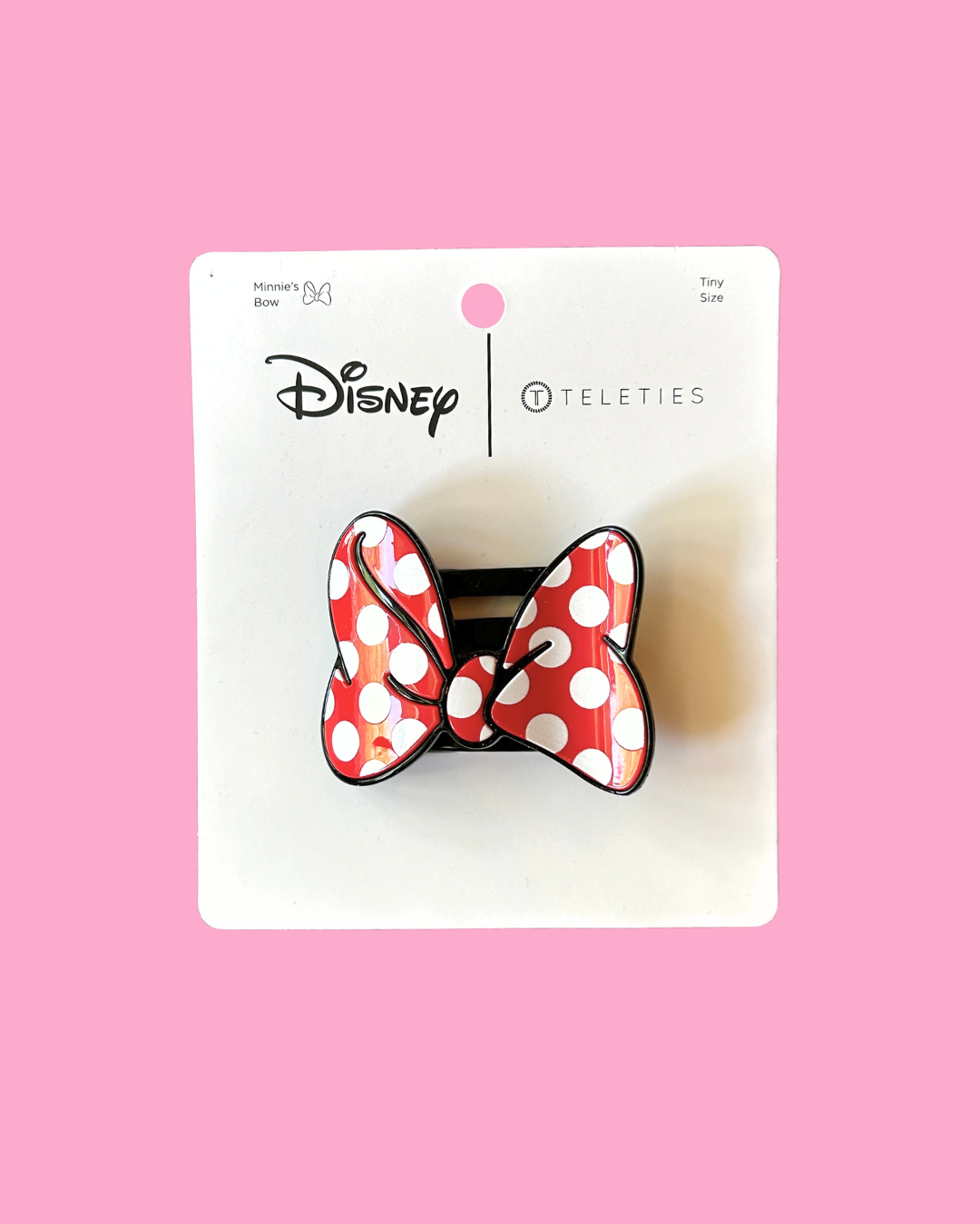 Red and white polka dot bow on a Disney branded card against a pink background