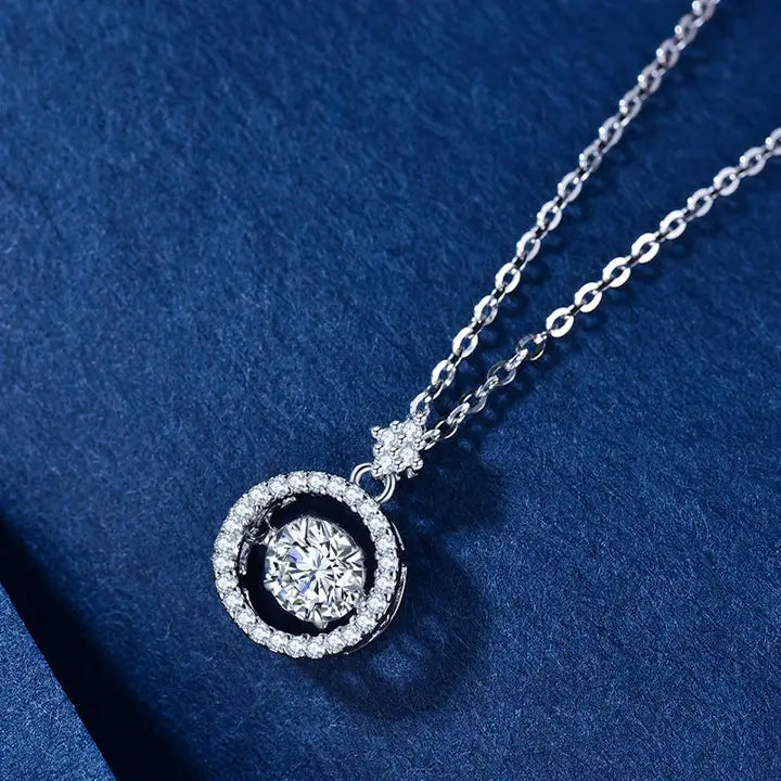 A silver necklace featuring a round moissanite charm with a hypoallergenic finish on a blue background.