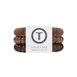 A set of four Teleties hair stretch bands in shades of brown, including solid medium brown, dark brown, and tortoiseshell patterns, wrapped around a white paper band with the Teleties logo.