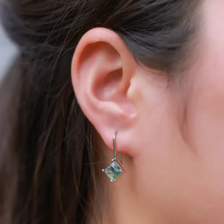 Close-up of an ear wearing a green gemstone earring with blurred hair and skin in the background