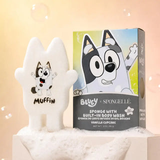 Bluey x Spongelle sponge with built-in body wash shown as a white Hamsa-shaped sponge labeled 'MUFFIN' next to its retail box featuring Bluey's character Bluey on a warm beige background with floating bubbles.