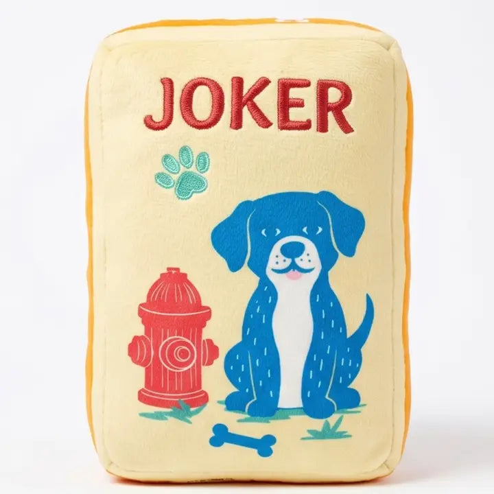 A square plush pillow with a cream-colored front, featuring an embroidered blue dog, red fire hydrant, and red &
