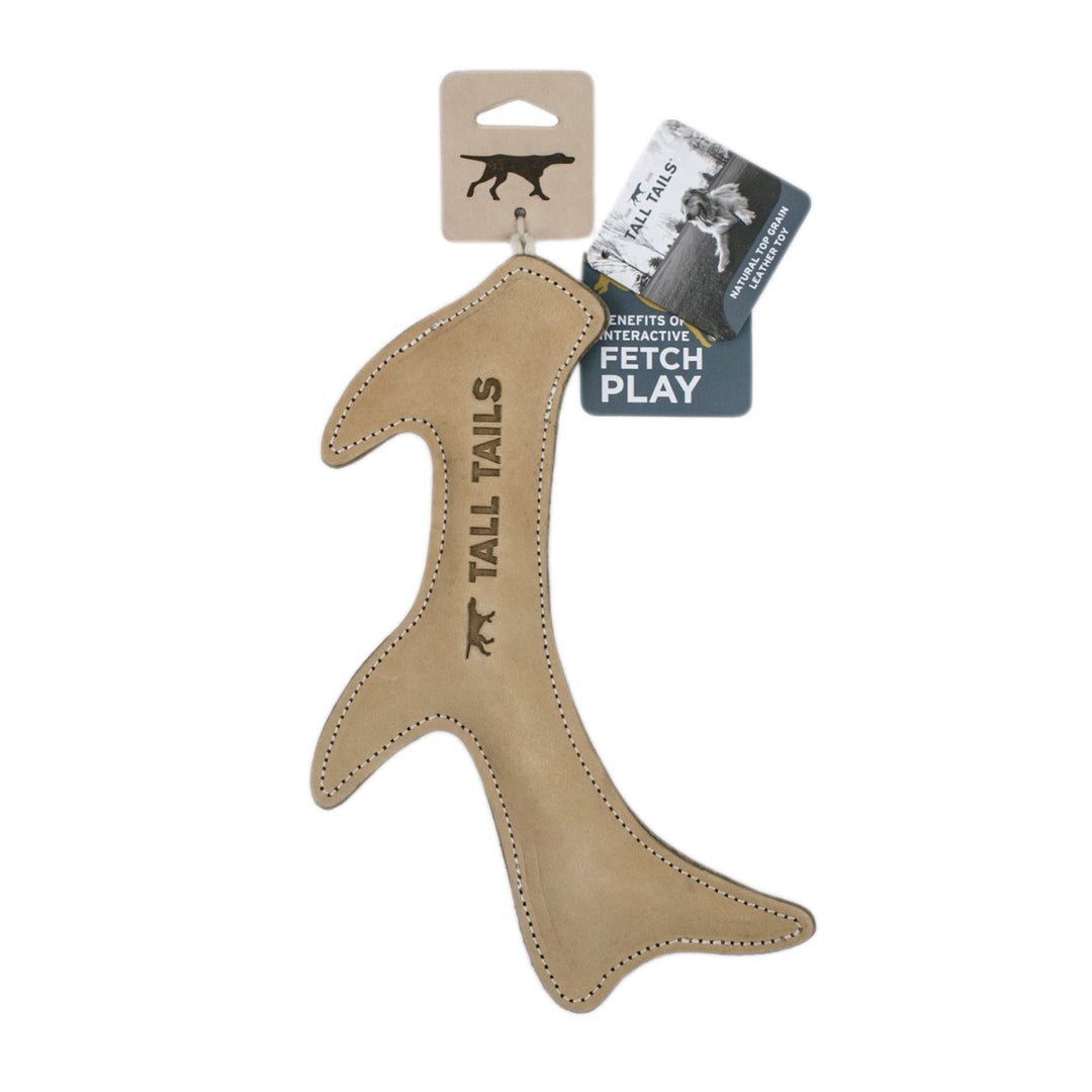 Tall Tails dog toy in tan faux leather, shaped like a stylized tail with stitched edges and laser-engraved branding, shown with its retail packaging on a white background.