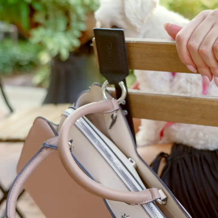 Close-up of a beige handbag with a black strap, blurred outdoor background