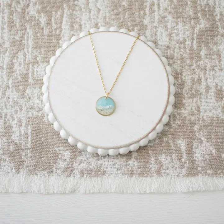 Necklace with a pendant on a white circular stand against a textured beige background