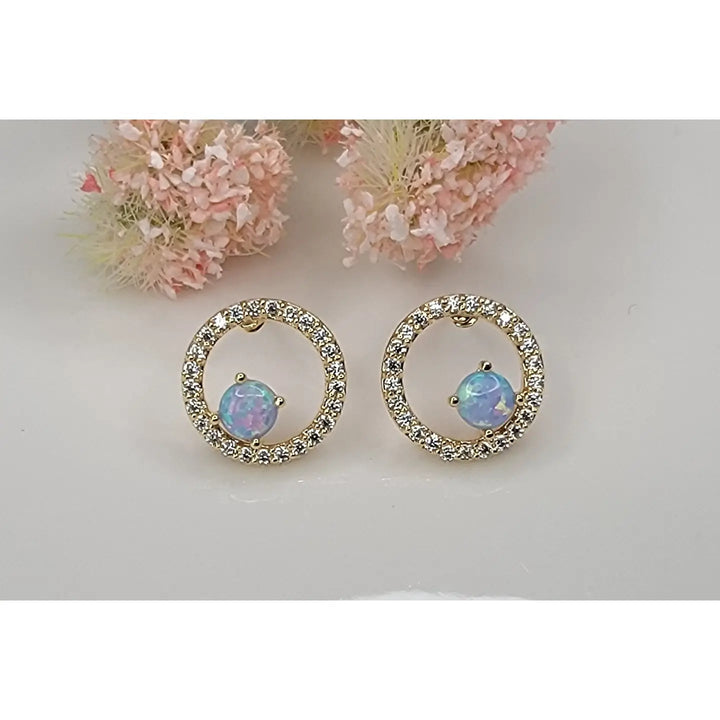 Pair of gold hoop earrings with opal stones on a light gray background with pink flowers.