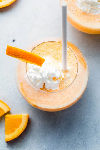 Orange smoothie with whipped cream and an orange slice on a gray surface