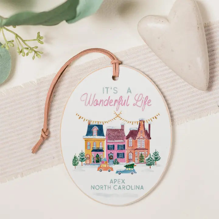 Decorative ornament with 'It's a Wonderful Life' text and houses illustration on a soft background.