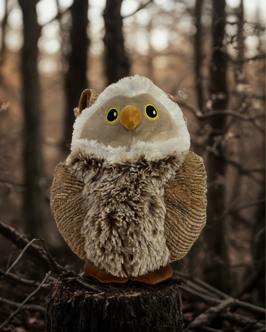 Plush owl toy on a stump in a forest setting