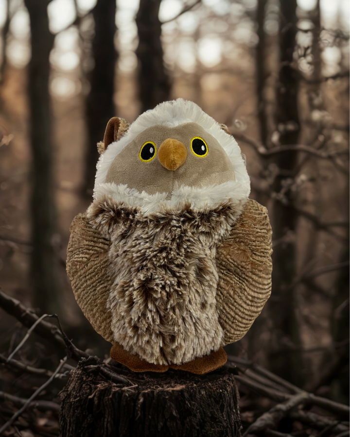 Plush owl toy on a stump in a forest setting