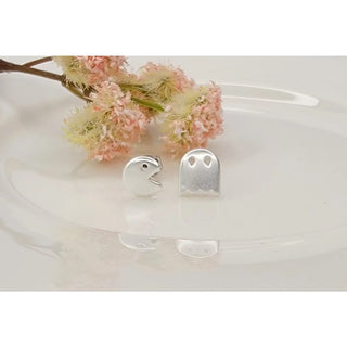 Silver ghost-shaped earrings on a white surface with pink flowers in the background