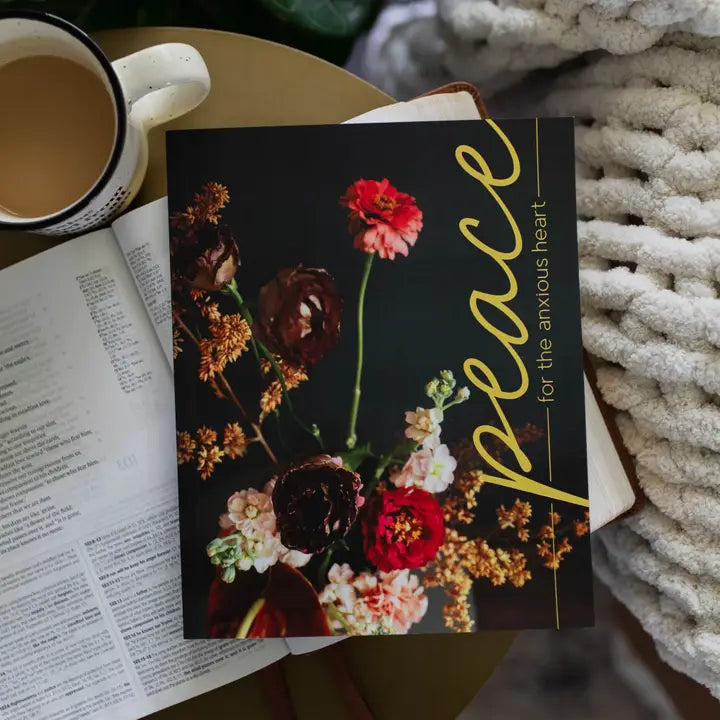 Book with floral cover titled 'Peace for the Anxious Heart' next to a cup of coffee on a textured surface.
