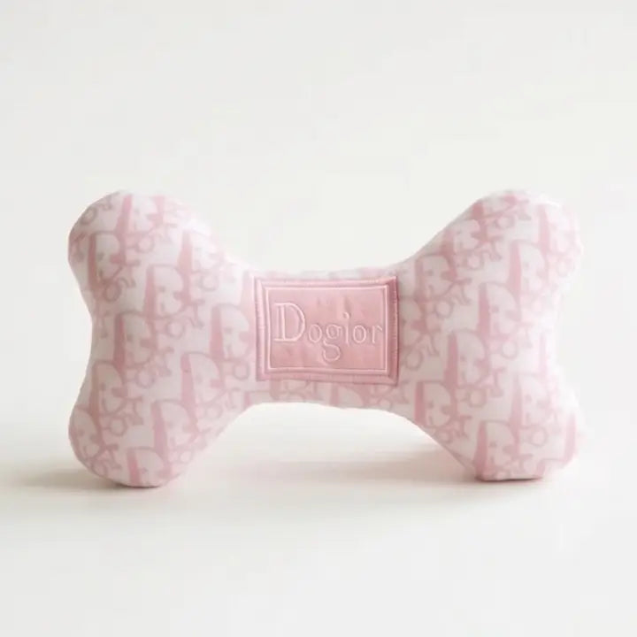 A bone-shaped dog toy in light pink and white with an allover monogram pattern and a central patch reading 'Dogion', photographed on a clean white background.