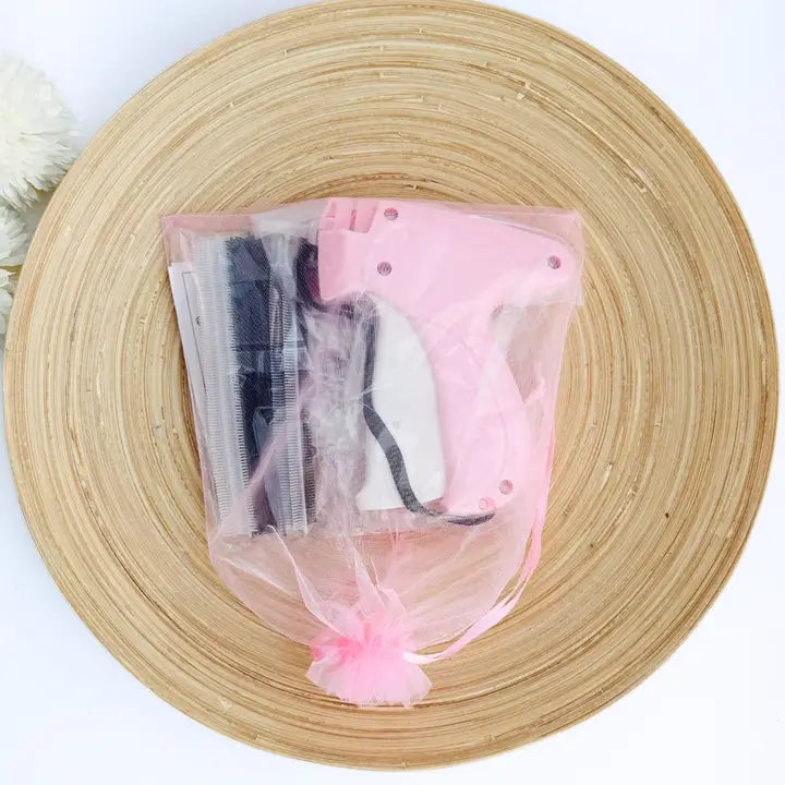 A pink hot glue gun inside a clear tulle drawstring pouch with a pink pom-pom, placed on a round woven bamboo tray against a white background.