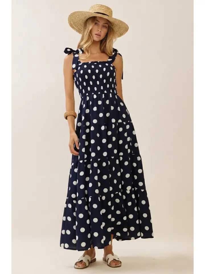 Woman wearing a navy blue dress with white polka dots and a straw hat on a beige background