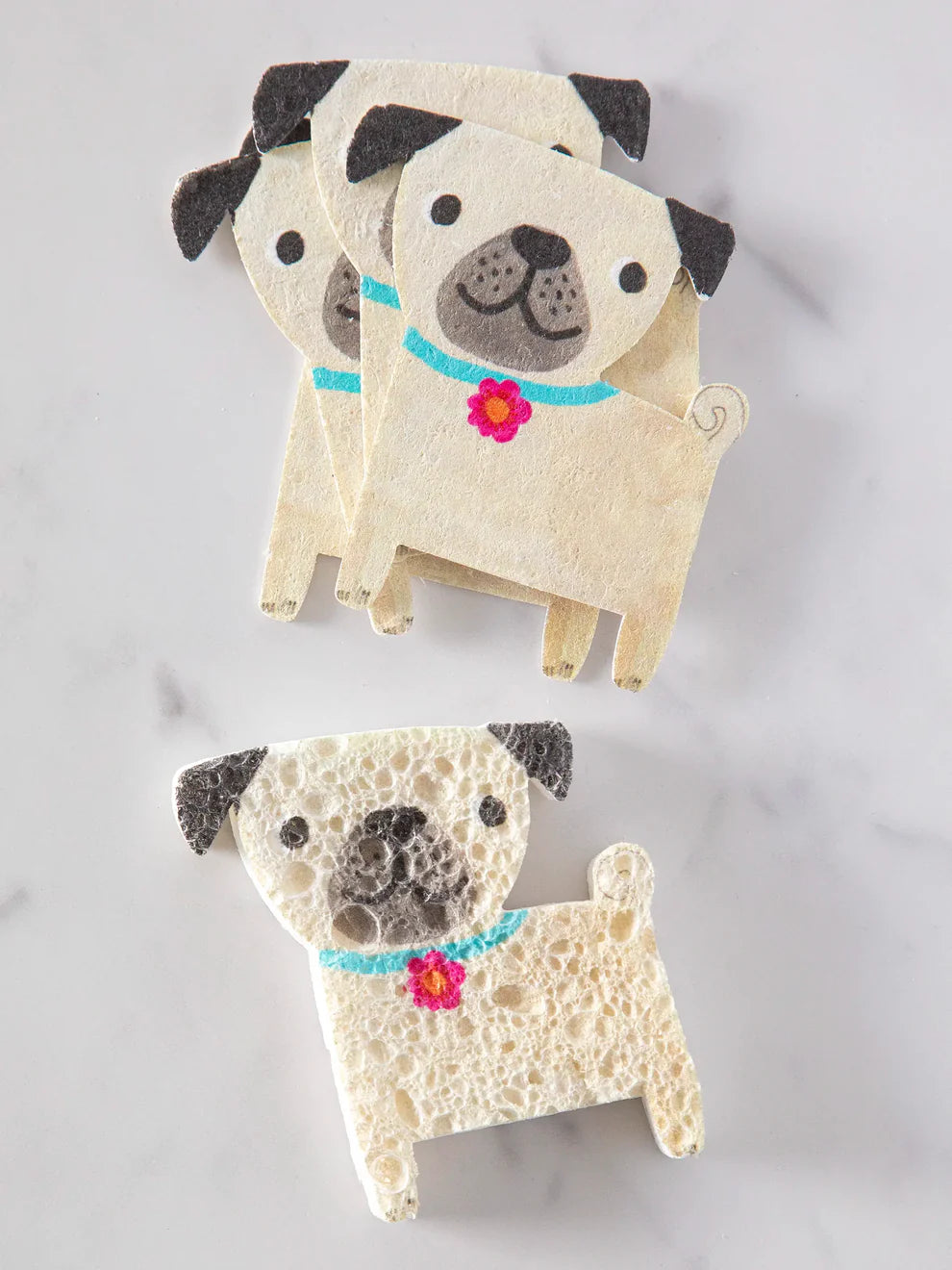 Three pug-shaped sponges with black and brown fur on a light gray background