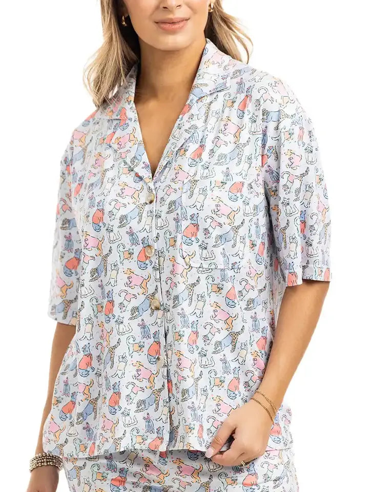 A woman wearing a short-sleeve button-front shirt and matching shorts set in a light blue and white patterned fabric with small multicolored illustrations, photographed against a plain white background.