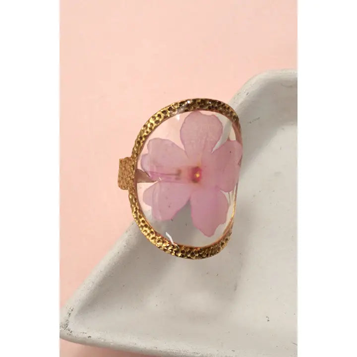 Ring with pink floral design and gold frame on a white surface with pink background