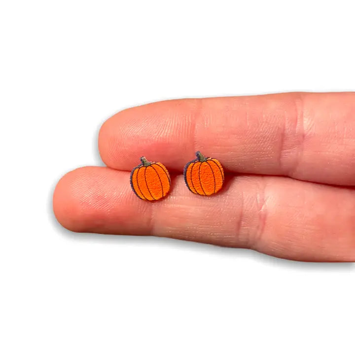 Pumpkin-shaped earrings held between two fingers on a white background